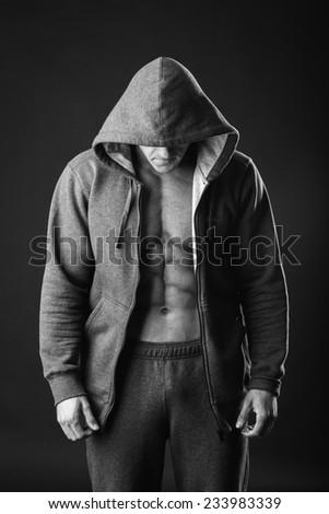 Young muscular man with open jacket revealing muscular chest and abs.Portrait of a muscular young man in hood jacket posing on black background.Young man with athletic body posing on black background