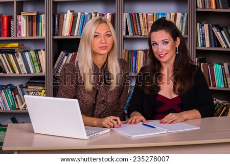 Young students, blond and brunetr works in the library. A young girls in their office, working on the computer. Study, computer, technology, student, students, beautiful girls.The concept of learning.