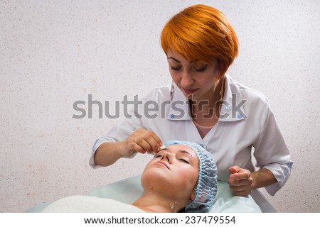 Therapist applying face mask to the face of a beautiful young woman using a cosmetic brush