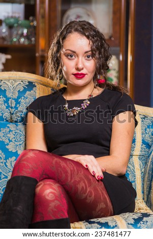 Portrait of beautiful romantic brunette on blue sofa. Professional make-up on a beautiful woman. A girl sits in a beautiful  sofa and looks enigmatically. Romantic, beautiful girl portrait.