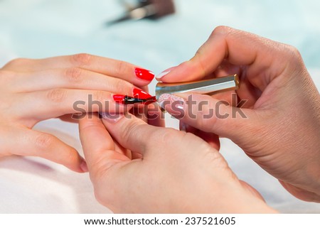 The process of doing a manicure in the spa salon. Applying red nail polish on the nails in the nail salon. Manicure, hand care, nail care, red lacquer. The concept of hand care, nail beauty.