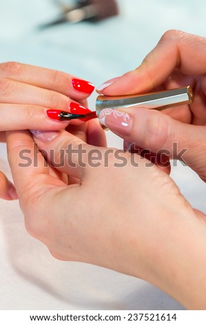 The process of doing a manicure in the spa salon. Applying red nail polish on the nails in the nail salon. Manicure, hand care, nail care, red lacquer. The concept of hand care, nail beauty.