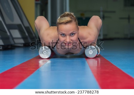 Woman push-ups on the floor.Gym woman push-up strength pushup exercise with dumbbell in a fitness workout. Athletic young woman doing exercises on the floor is pushed.