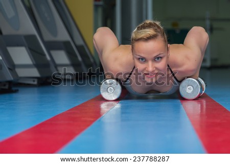 Woman push-ups on the floor.Gym woman push-up strength pushup exercise with dumbbell in a fitness workout. Athletic young woman doing exercises on the floor is pushed.