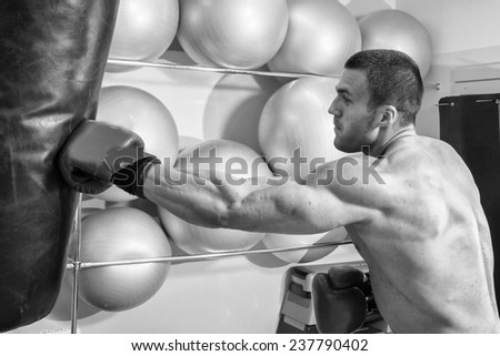 Muscular man in the gym. The man in boxing gloves, hit a punching bag, exercise. Boxing, workout, muscle, strength, power - the concept of strength training and boxing
