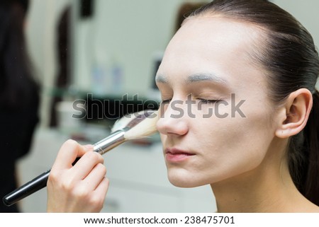 Application of powder on the model\'s face. Makeup artist in a beauty salon doing make-up special brush. Dressing room, a white powder, creativity and beauty.