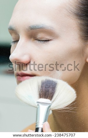 Application of powder on the model\'s face. Makeup artist in a beauty salon doing make-up special brush. Dressing room, a white powder, creativity and beauty.