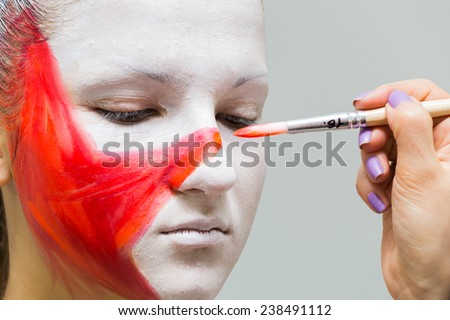 Putting drawing on the model\'s face. Makeup artist draws a star on  face of the model with a brush. Red star on face, creativity, make-up, the idea, brush, creative process.