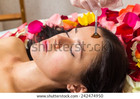 The girl lays on petals in spa salon. Brunette relaxed and waiting for the beginning of the spa treatments. Application of peeling on the girl\'s face. Facial treatment, rejuvenation, facial.