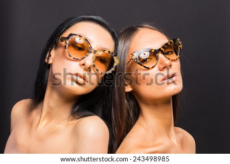 Two beautiful girl in sunglasses posing in the studio. Using advertising sunglasses. Two brunette in sunglasses.
