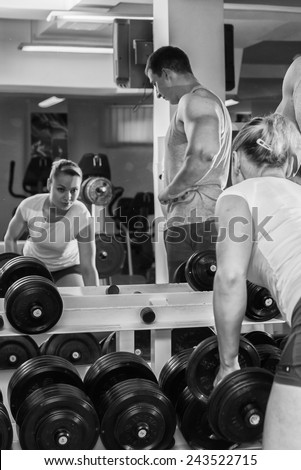 The coach with the client in the gym. Sports man and athletic girl involved in fitness in the gym. Beautiful blonde doing exercises with dumbbells.