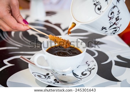Coffee from a beautiful black and white teapot, pour into a cup on the table designer. Stick with sugar remain in the cup. Coffee, tea, mug, pour, caffe - the concept of catering.