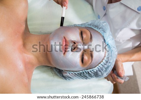 Applying cosmetic cream treatment on  face in spa salon. Beautiful young woman during facial treatment in cosmetic salon close up.