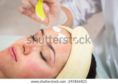 Applying cosmetic cream treatment on  face in spa salon. Beautiful young woman during facial treatment in cosmetic salon close up.