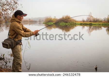Young fisherman fishing on the river bank. Professional fisherman holding a spinning fish on a hook. Playing a fish. The concept of a country holiday.