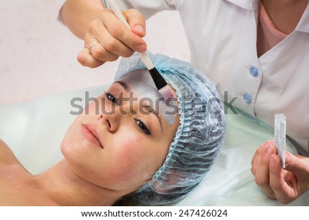 Beautician working on a face model in a spa salon. The process of cosmetic facial treatments. Beautician applying mask on the face of the model. Rejuvenation, skin nutrition.