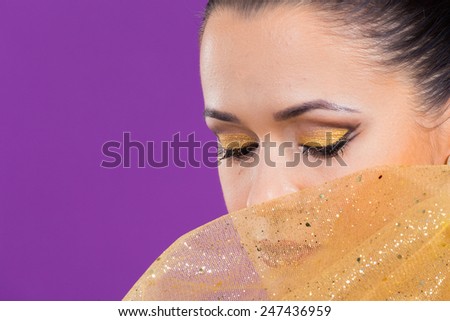 Girl with a professional makeup posing on a purple background. Beauty photo. Gold cloth near the girl\'s face. gold fabric, cloth. Makeup executed in gold style.The perfect make-up lips and eyes