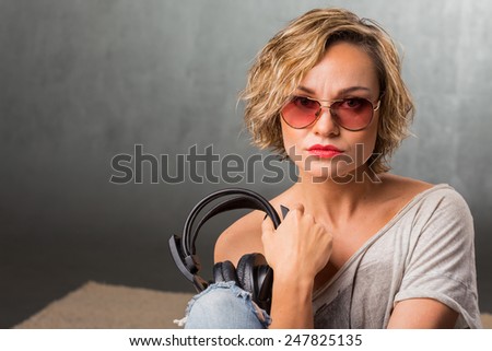 Blonde in headphones. Stylish girl in casual clothes on a gray background. Blonde posing in the studio.