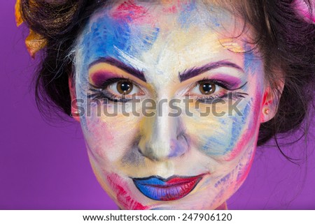 Beauty model on a purple background. Creative floral make-up on the face of the model. Multi-colored roses in her hair. Colorful makeup. Art make-up face, lips, eyes and hair.