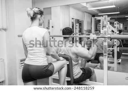 The coach with the client in the gym. Sports man and athletic girl involved in fitness in the gym. Muscular man working out with weights