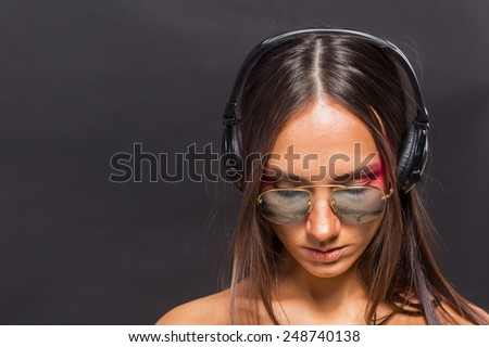 Brunette in sunglasses and headphones on a dark background. Sad sad music evokes emotions. Music, headphones, mood, emotion, enjoyment of music.