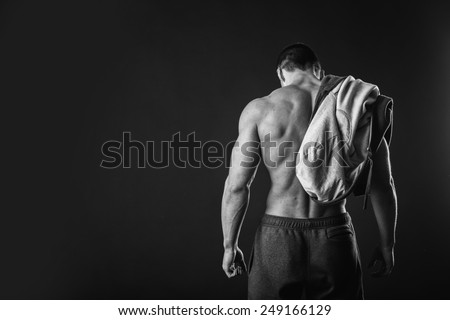 Handsome, muscular man in sportswear posing on a dark background. Confident man in an unbuttoned jacket. Bodybuilder man in  sports jacket.