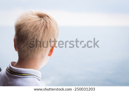 The boy looks at the sea from the deck of the ship. Boy with blond hair in a good mood on the deck, watching the sea.Sea voyage.