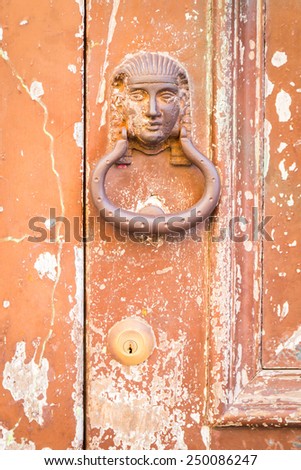 The old door handle in the form of the pharaoh on the old cracked door. Texture of old painted wood.