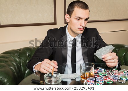Poker player in the casino with glass of whiskey and cards at the gaming table