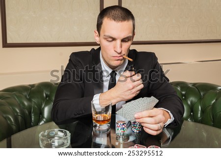 Poker player in the casino with glass of whiskey and cards at the gaming table