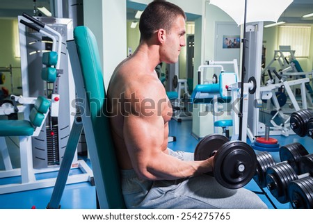 Muscular man working out with weights in gym. Man makes exercises.