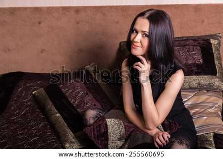 Portrait of a beautiful brunette. Portrait of a girl in a bedroom in chocolate tones. Girl holding an embroidered pillow. The concept of beauty and relaxation.