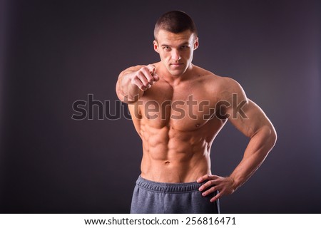 Young bodybuilder guy in good shape against a dark background. Man posing, showing his muscle definition.