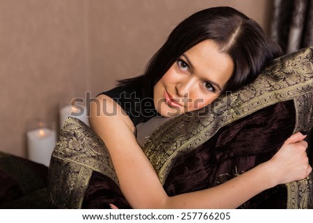 Portrait of a beautiful brunette. Portrait of a girl in a bedroom in chocolate tones. Girl holding an embroidered pillow. The concept of beauty and relaxation.