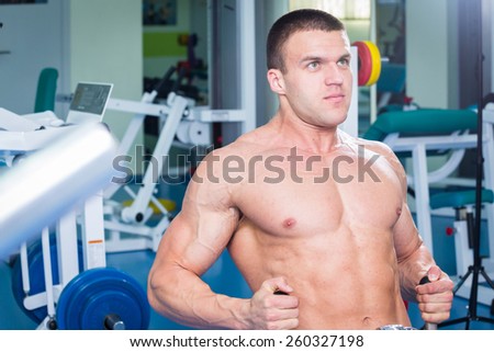 Fit man exercising at the gym on a machine.Man at the gym. Man makes exercises. Sport, power, dumbbells, tension, exercise - the concept of a healthy lifestyle. Article about fitness and sports.