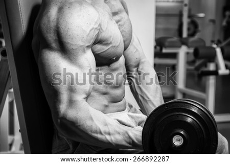 Handsome and strong man with beautiful body doing exercises in gym