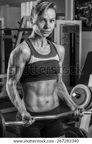Female fitness. Blonde with a perfect figure, training in the gym. Athletic girl delat exercises with barbell. Strength training.