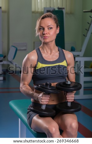 Beautiful, sexy, muscular blonde in the gym. Female fitness. Girl posing in the gym. Fitness woman doing exercises with dumbbells in the gym. Sports, bodybuilding. Attractive woman in the gym