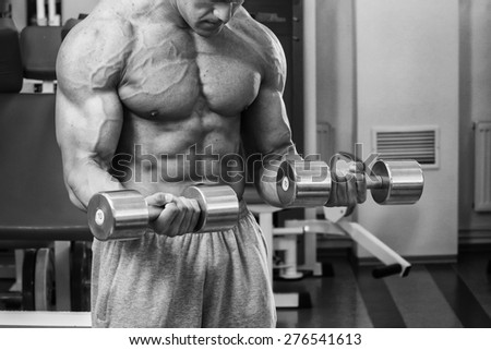 Strong beautiful man, pumping biceps. Training biceps dumbbells. Bodybuilder trains the muscles of the arms.