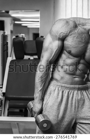 Strong beautiful man, pumping biceps. Training biceps dumbbells. Bodybuilder trains the muscles of the arms.