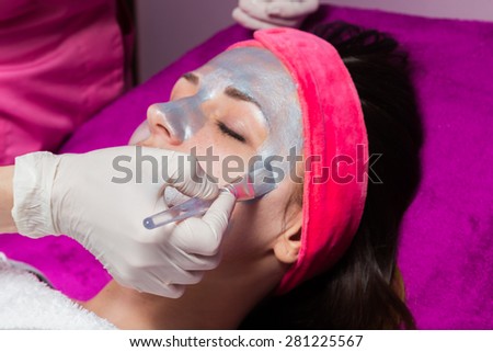 Facial Skin Care. Drawing a silver mask on the face of a beautiful girl. Anti-aging facial mask.