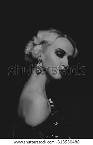The blonde in a black dress on a dark background. Model in a beautiful black dress. Beautiful blonde on a dark background. Black and white photo. Jewelry\'s extraordinary. Design stylish way to model.