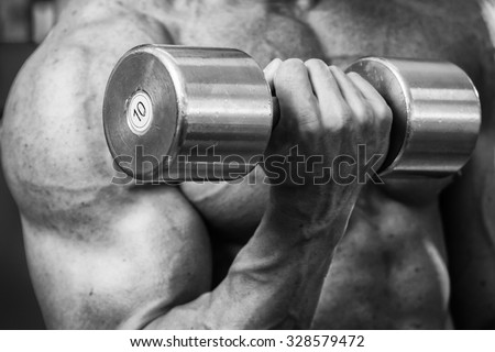 Bodybuilder makes exercise with dumbbells at the gym. Work on hands tell muscles. Exhausting workouts to an end. Photos for sporting magazines and websites.