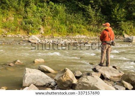 Fisherman on a mountain river catch exotic fish. Trout fishing in the Carpathian rivers. Untouched nature of the mountains. Photo for fishing and Natural magazines, posters and websites.