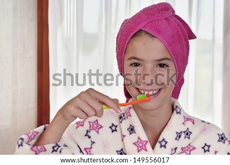 Young woman brushing teeth in bath robe with towel on head in bright bathroom
