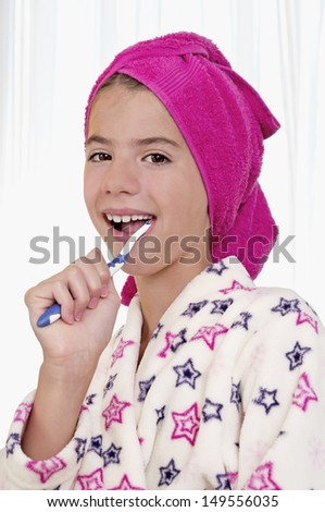 Young woman brushing teeth in bath robe with towel on head in bright bathroom