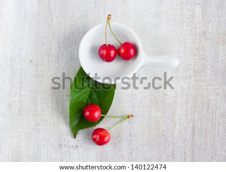red sweet cherry in the white gravy boat and green leaf