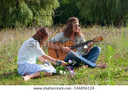 young hippie men play on the guitar and sing, young hippie women twine a wreath with flowers