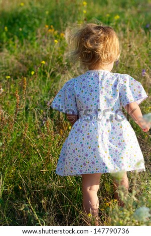small girl in the light dress in the middle of the summer grass