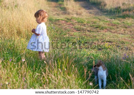 small girl in the light dress and cat is taking a walk